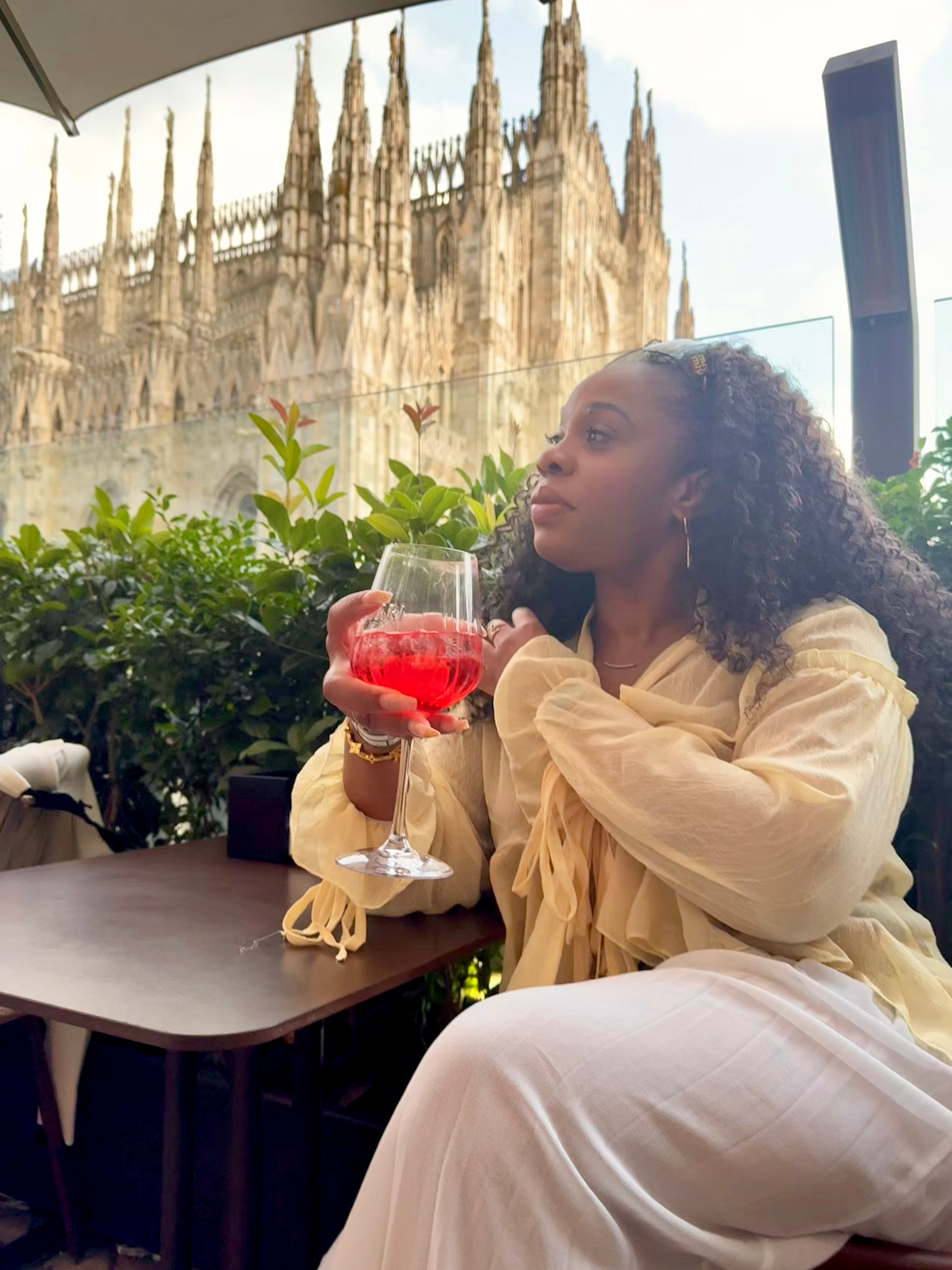 Woman holding a glass of pink drink with a cathedral in the background